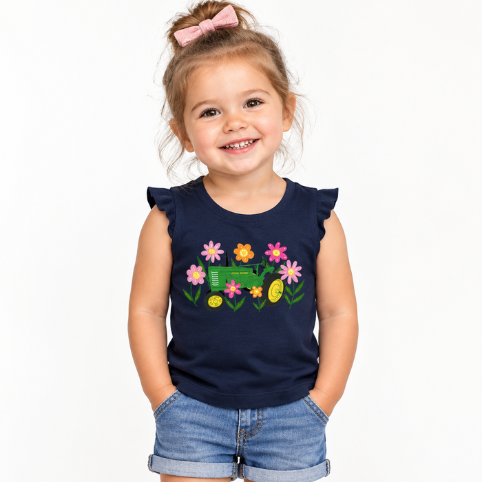 A young girl with a pink bow in her hair is smiling and wearing a navy blue sleeveless top with a colorful graphic of a green tractor, flowers, paired with denim shorts, against a plain white background. John Deere Toddler Girls Flowers & Tractor Tank