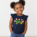 A young child with curly hair in pigtails wearing a John Deere Toddler Girls Flowers & Tractor Tank, paired with blue jeans, standing against a plain white wall.