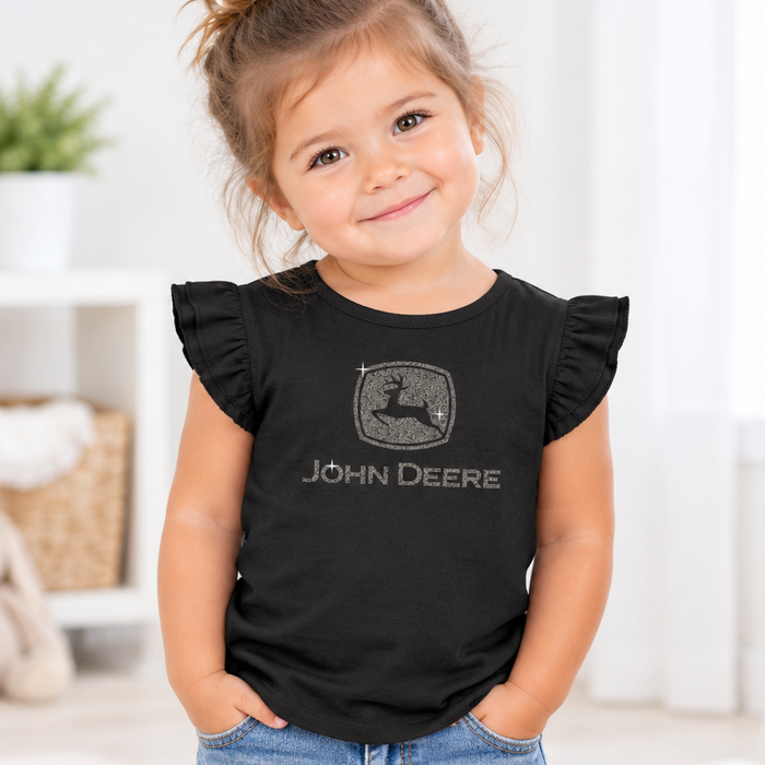 A young girl with her hair in a bun wearing a black short-sleeve t-shirt with ruffled sleeves. The shirt features a distressed gray John Deere logo and brand name on the chest.