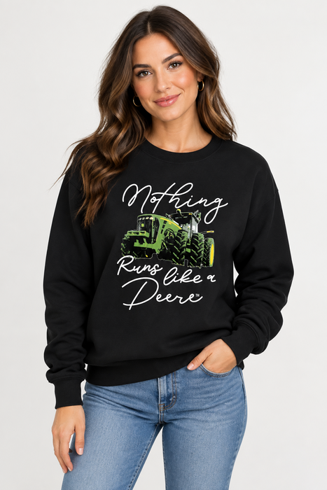 A woman wearing a black John Deere Ladies "Nothing Runs Like a Deere" Crew Fleece  with a green tractor graphic and the text 'Nothing Runs like a Deere' in white script, paired with blue jeans, against a light gray studio background.
