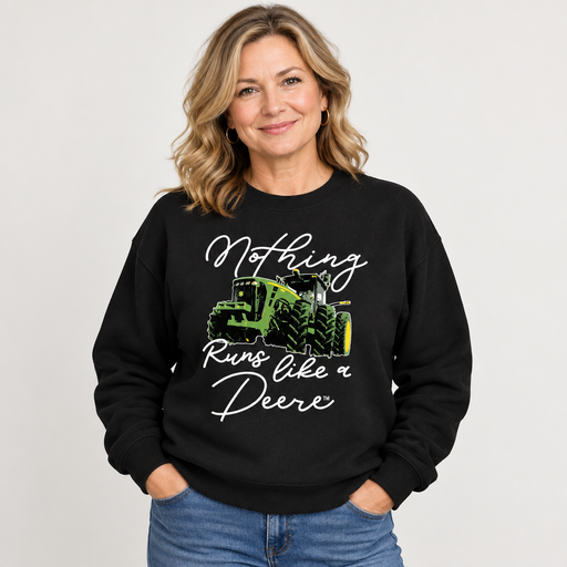 A woman wearing a black crewneck sweatshirt with a graphic of a green John Deere tractor and the text 'Nothing Runs like a Deere' in white script, paired with blue jeans, against a light gray background. John Deere Ladies "Nothing Runs Like a Deere" Crew Fleece