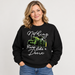 A woman wearing a black crewneck sweatshirt with a graphic of a green John Deere tractor and the text 'Nothing Runs like a Deere' in white script, paired with blue jeans, against a light gray background. John Deere Ladies "Nothing Runs Like a Deere" Crew Fleece