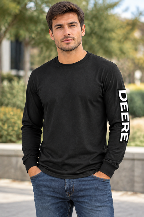 A man wearing a black long-sleeve crewneck shirt with 'DEERE' printed vertically in white on the right sleeve, paired with blue jeans, standing outdoors.