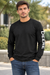 A man wearing a black long-sleeve crewneck shirt with 'DEERE' printed vertically in white on the right sleeve, paired with blue jeans, standing outdoors.