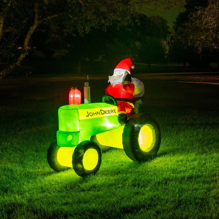 An inflatable yard decoration featuring Santa Claus sitting on a tractor with a John Deere logo, illuminated by LED lights in a dark yard.